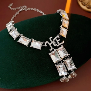 Detailed close-up of crystal necklace with square pendant and HE initials on velvet