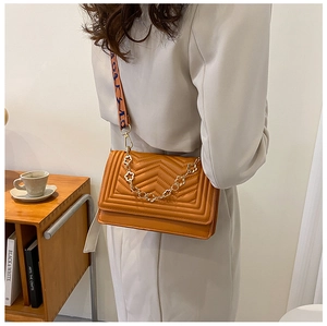Detail of caramel crossbody bag with V-quilted texture and gold floral chain accessory