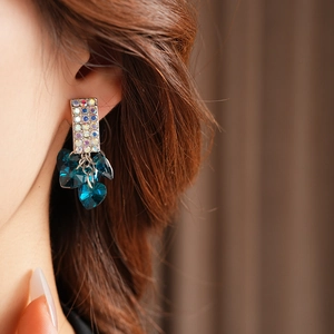 Detail of square rhinestone earrings with heart-shaped blue crystals worn by a model