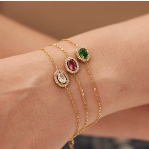 Wrist-worn view of three gold bracelets featuring red, green, and white zircon gemstones