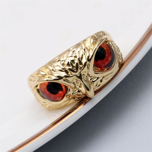 Macro detail of owl ring with gold relief texture and vibrant red zircon eyes