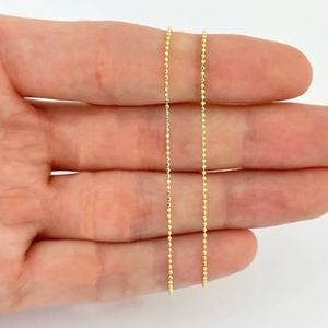Detailed view of an ultra-fine golden bead chain necklace held to show its delicate texture