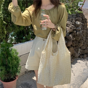 Close-up of cream lace texture tote bag held against casual summer outfit outdoors