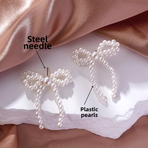 Detail of white faux pearl bow earrings with steel needles on rock and satin
