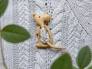 Detail of a handmade wooden mouse brooch pinned on grey knit fabric with leaf accent