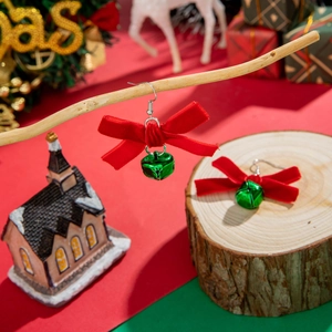 Detailed close-up of red velvet bow and green bell Christmas earrings on festive decor