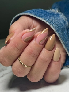 Macro detail of long almond nails in nude pink with gold waves and sparkling glitter