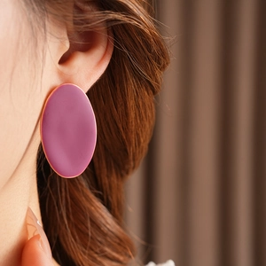 Primo piano di un orecchino ovale in smalto viola con bordo dorato indossato da una modella
