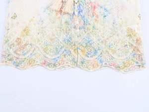 Détail de l'ourlet brodé avec imprimés floraux et pompons sur le chemisier de couleur crème