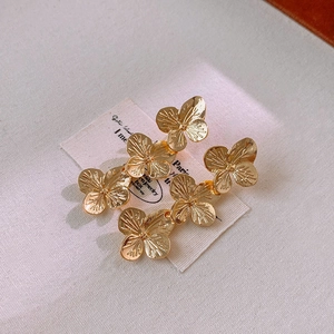 Macro view showing the intricate layered petals of golden floral earrings on a soft fabric