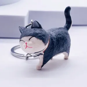 Close-up of cute black and white cat keychain with red collar and bow on white background