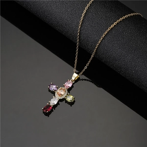 Luxurious gold-tone necklace with a colorful gemstone cross pendant on a sleek black surface