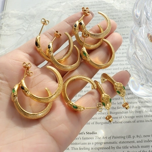 Dettaglio di orecchini a cerchio a serpente placcati oro 18K con pietre verdi sulla mano