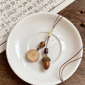 Artistic detail of vintage wax cord necklace with wooden acorn pendant on ceramic dish