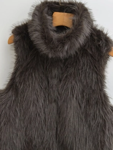 Detailed texture of dark grey faux fur vest hanging on a wooden hanger with white background