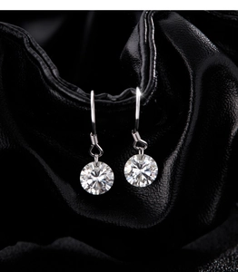 Détail macro des boucles d'oreilles en argent moissanite sur fond cuir noir plissé