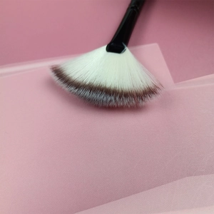 Macro di un pennello a ventaglio con setole sfumate marroni su sfondo di carta rosa