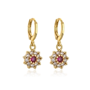 Macro view of gold flower earrings with central red gemstone and zircon accents