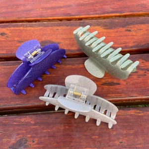 Close-up of three glittery acetate hair claws in purple, light green and silver colors