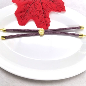Detail of purple braided bracelet with gold tree of life charm on white tray