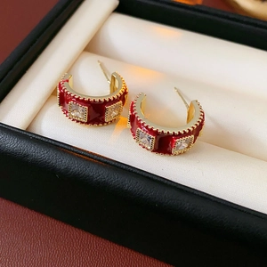 Macro shot of gold-plated C-shape earrings with red enamel and inlaid square zircons