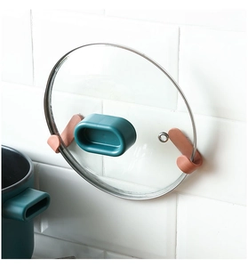 Detail view of brick red J-shaped wall hooks holding a glass pot lid on kitchen tiles