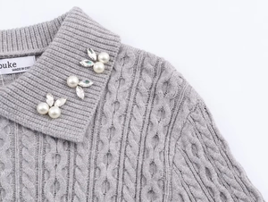 Detalle del cuello de un jersey gris de punto trenzado con perlas y adornos de hojas de cristal