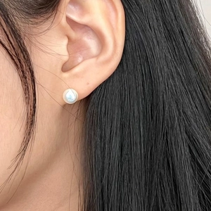 Close-up of minimalist round shell pearl earrings on model showing pearlescent luster