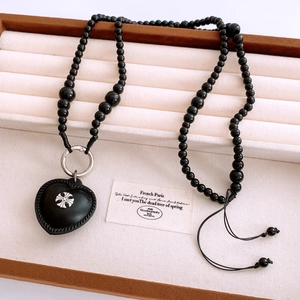 Close-up of black beaded necklace with leather heart pendant and metal cross detail