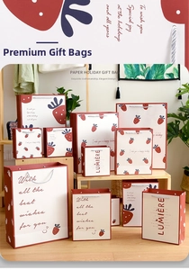 Detailed view of various sizes of strawberry printed gift bags with white rope handles
