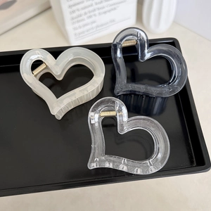 Three heart-shaped hair clips in clear, cream, and smoky grey on a minimalist black tray