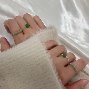 Detail of four thin gold and silver rings with green pearls worn on fingers