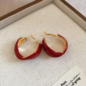 Close-up of red enamel and gold-plated C-shaped earrings on textured beige background