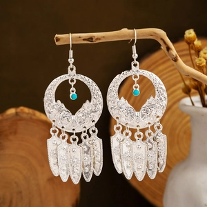 Ethnic style long silver tassel earrings with turquoise beads hanging on a rustic wood branch