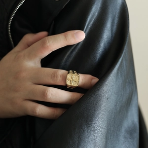 Close-up of a gold cross ring with stone texture worn on a hand with black leather