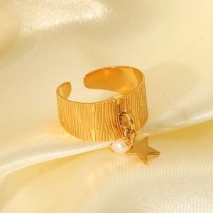 Close-up of gold star pendant and pearl on textured open ring against yellow silk