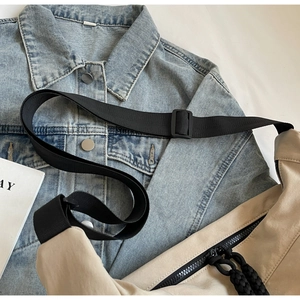 Detail of light beige casual crossbody bag with black adjustable strap on denim jacket