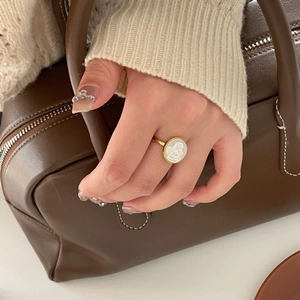 Close-up of vintage gold ring with oval shell relief worn against a stylish knit sweater