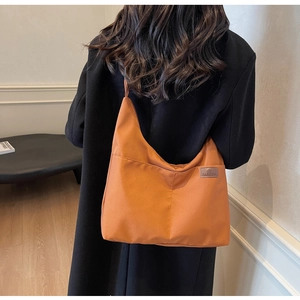 Close-up of orange waterproof nylon tote bag with leather logo patch on model's shoulder