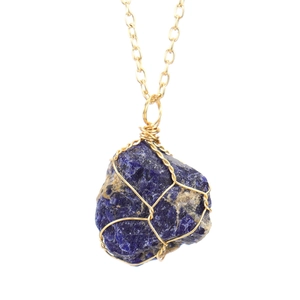 Macro detail of handmade gold wire-wrapped deep blue natural crystal stone pendant