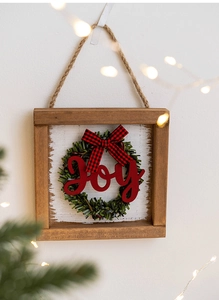 Detail of wooden Christmas door sign with Joy letters and green wreath hanging on white wall