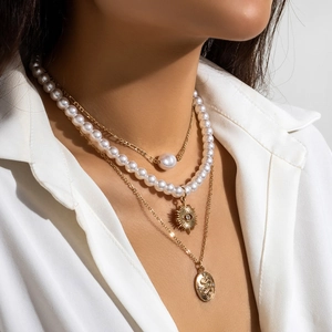 Detail of layered gold necklaces with pearl charms and sun pendants on white shirt