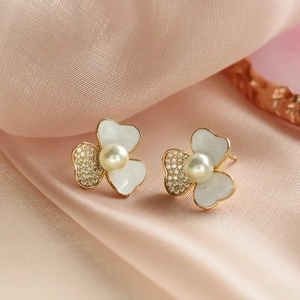 Three-petal floral pearl studs with white enamel and crystals on pink silk background