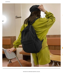 Detail showing the large capacity black nylon backpack worn by a model in a cafe setting