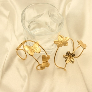 Detailed top view of 18k gold butterfly and flower open bangles on beige silk