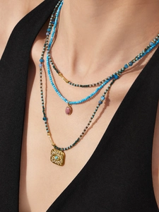 Detail of layered turquoise beaded necklace with gold Evil Eye pendant and pink gemstone
