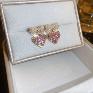 Close-up of heart-shaped pink crystal earrings with pearl bow and gold metal plating