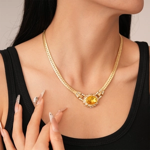 Detail view of gold snake chain necklace with oval yellow gemstone and crystal accents