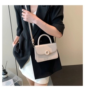 Close-up of cream crossbody bag with gold round buckle being held by a model