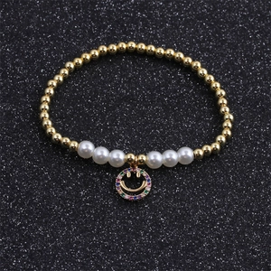 Detail of gold beaded bracelet with white pearls and a colorful zircon smiley charm